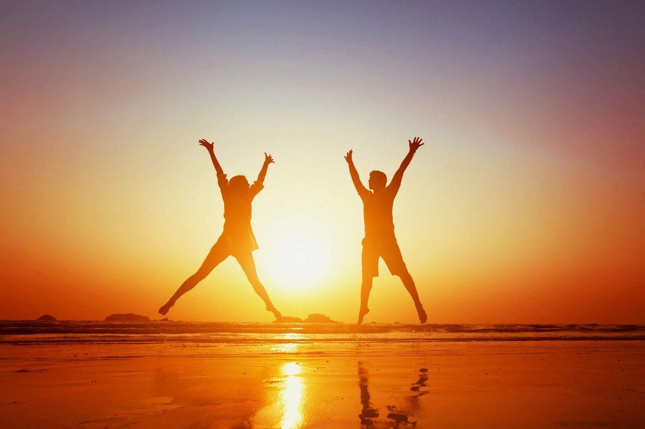 Two silhouetted figures jumping on a beach at sunset