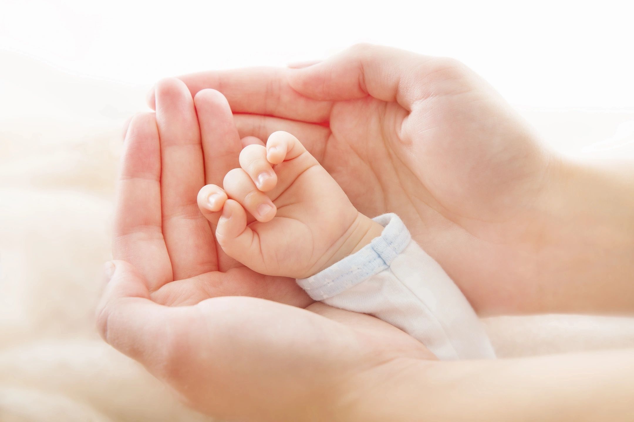 A baby hand cradled in adult hands