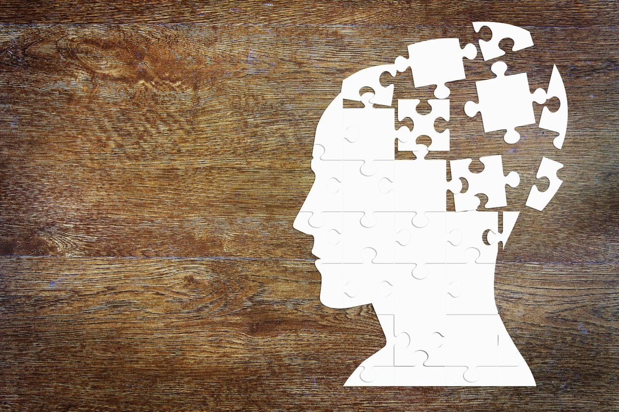 White puzzle-piece head silhouette on a wooden background